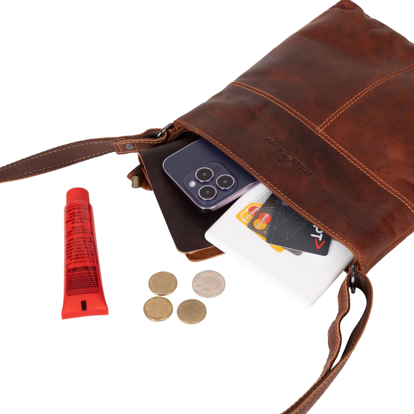 Brown leather crossbody bag with phone, cards, and coins on a white background