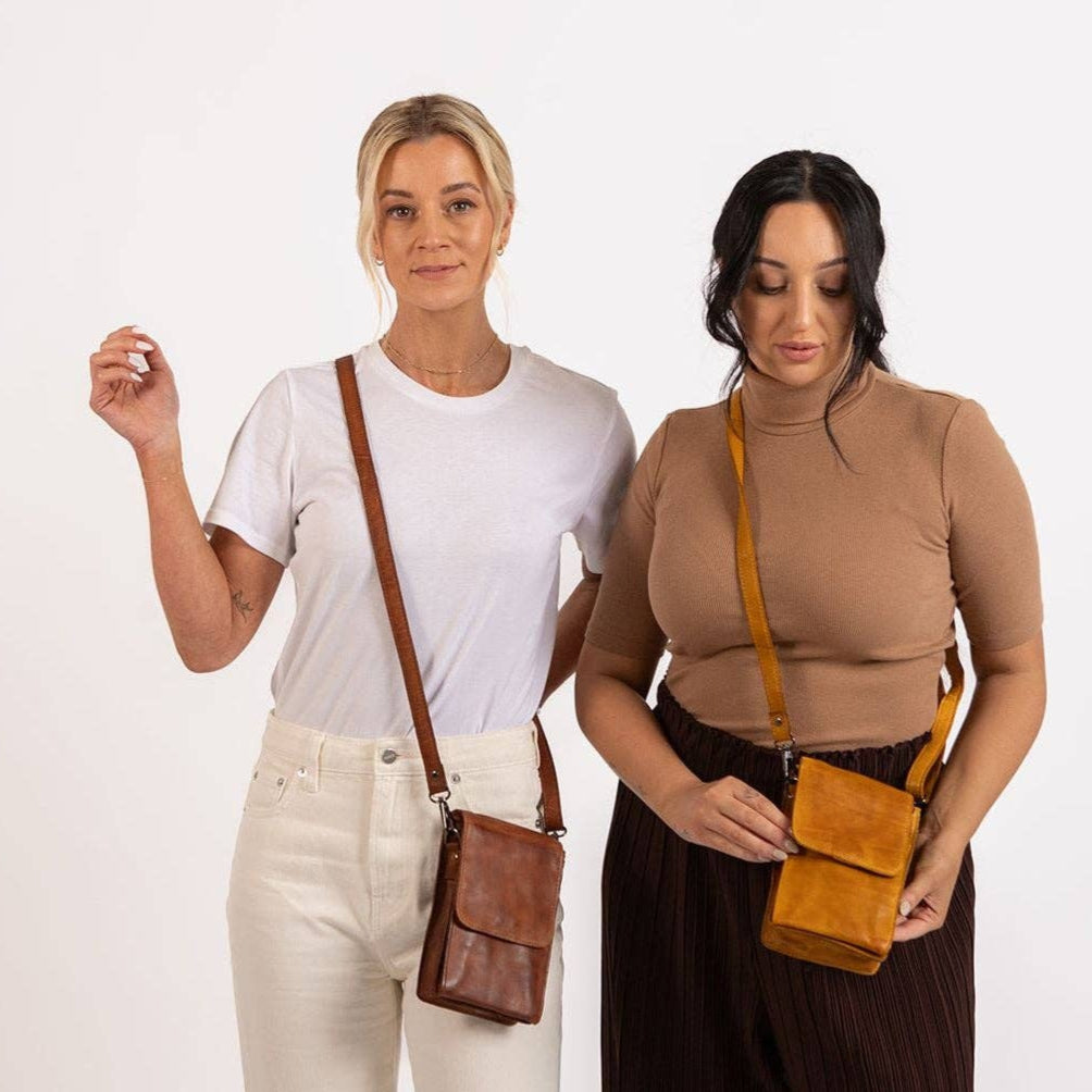 Two women holding brown crossbody bags against a white background
