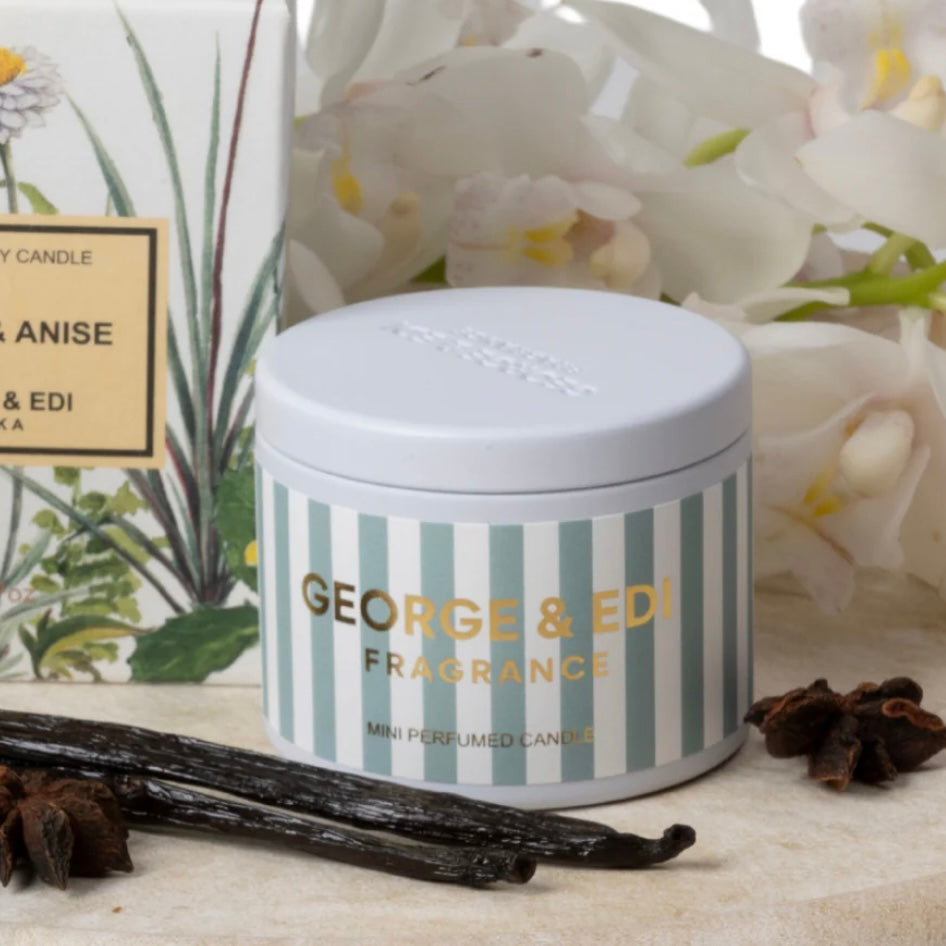 Striped candle container with 'George & Edi' branding on a surface with vanilla beans and flowers.