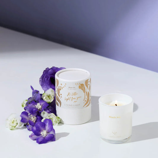 White candle with a decorative label and purple flowers on a light background