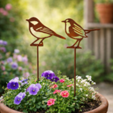Two metal bird sculptures in a pot of flowers with a blurred garden background