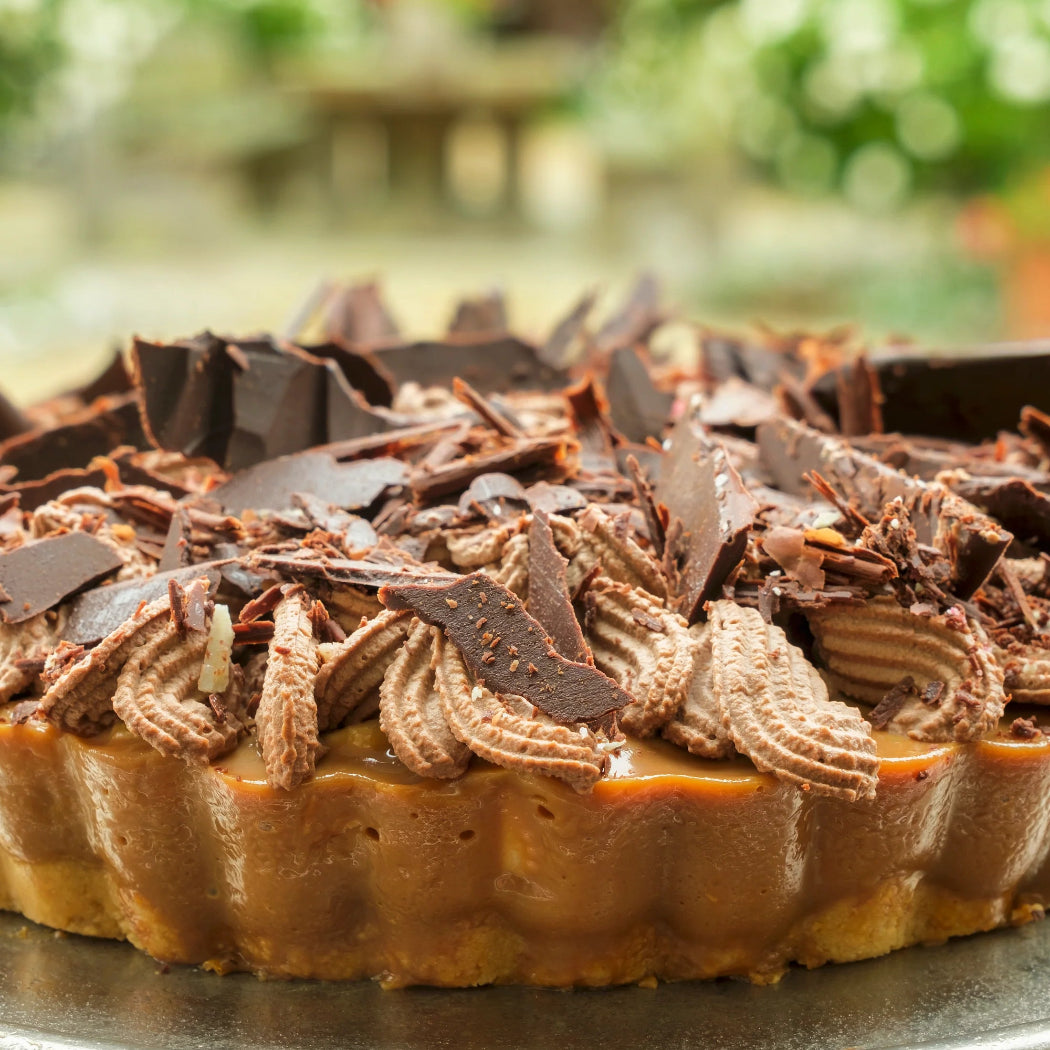 Chocolate-topped tart on a metal stand with a blurred garden background