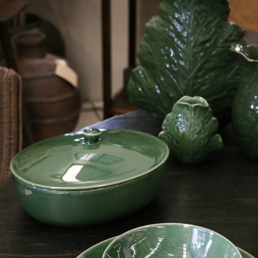 Green ceramic dish set on a wooden surface with decorative leaves.