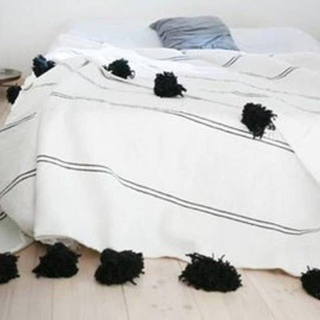 Bed with white comforter and black pom-poms in a minimalistic room.