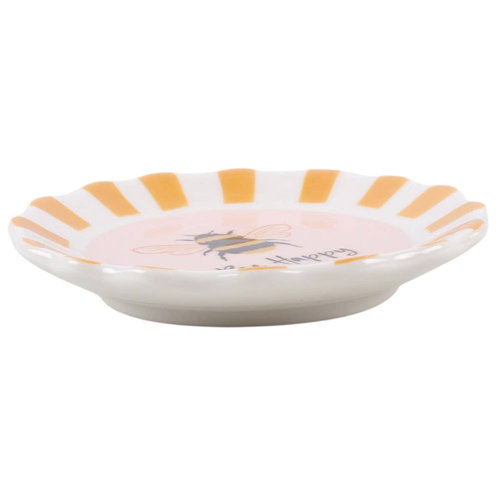 A small white ceramic dish with a scalloped rim featuring alternating orange and yellow stripes, a pink center, a bee illustration, and the word 'Happiness' in script.