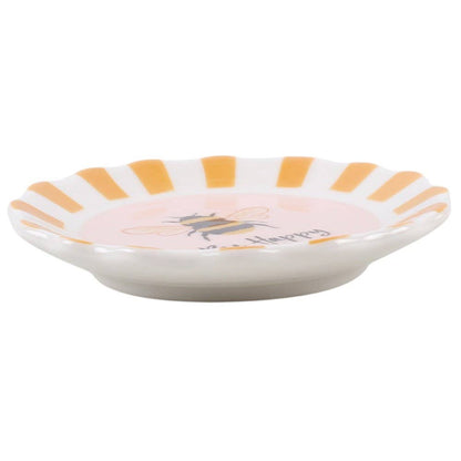 A small white ceramic dish with a scalloped rim featuring alternating orange and yellow stripes, a pink center, a bee illustration, and the word 'Happiness' in script.