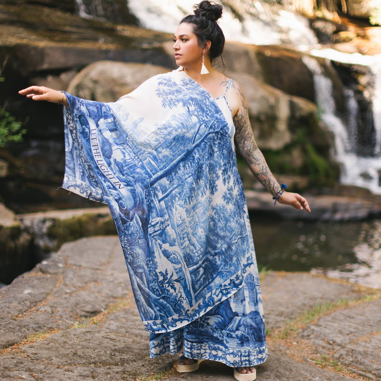 Woman in a blue and white patterned dress standing in front of a waterfall.