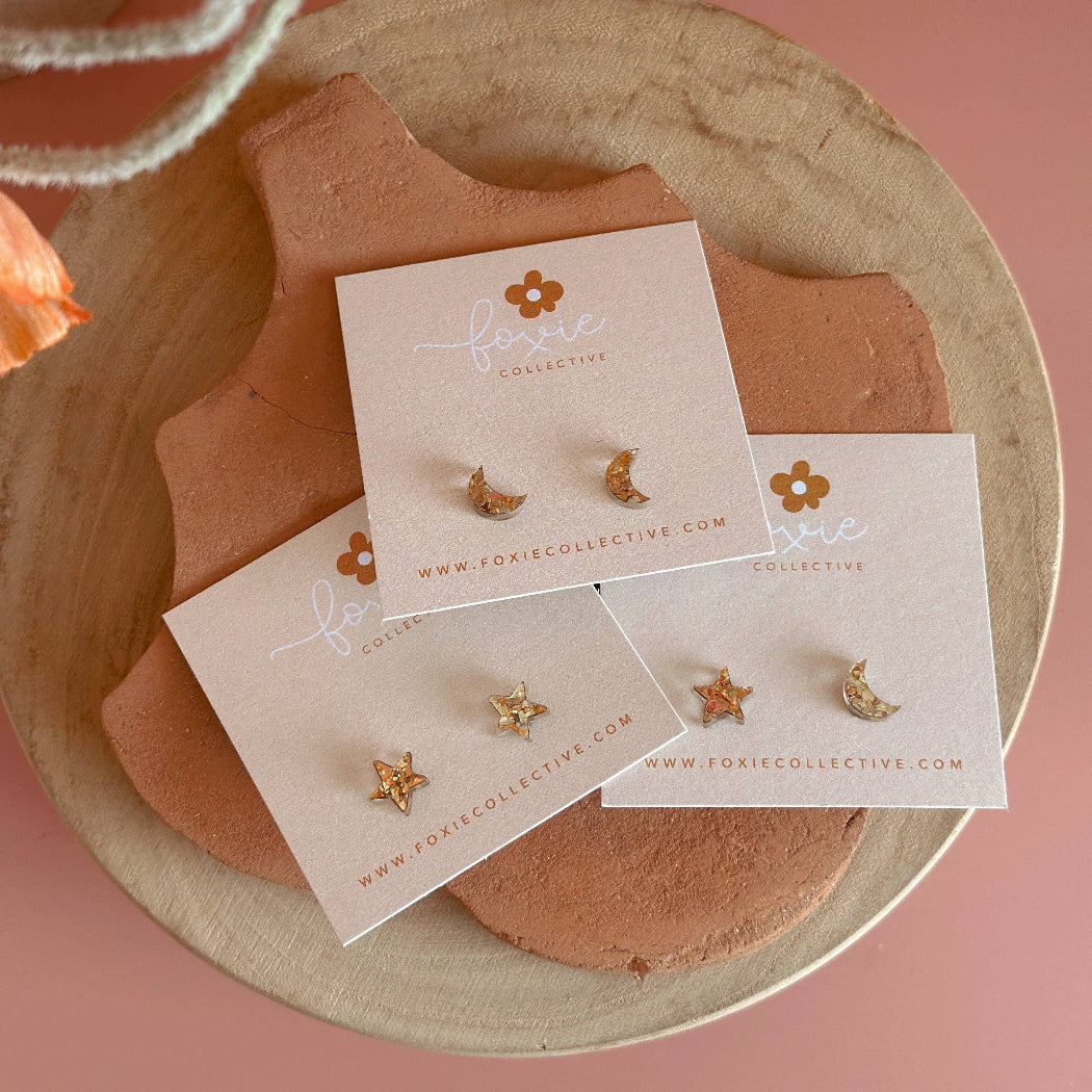 Gold earrings on a branded card with a floral background