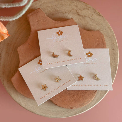 Gold earrings on a branded card with a floral background