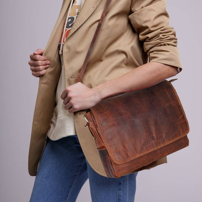 Person holding a brown leather satchel bag against a plain background