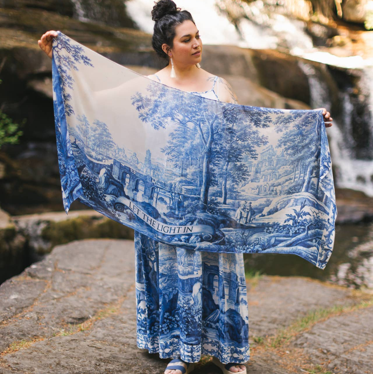 Woman holding a blue and white patterned scarf in front of a waterfall