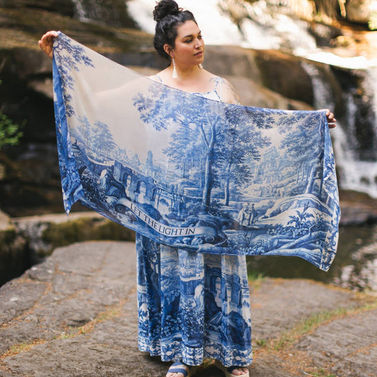 Woman holding a blue and white patterned scarf in front of a waterfall