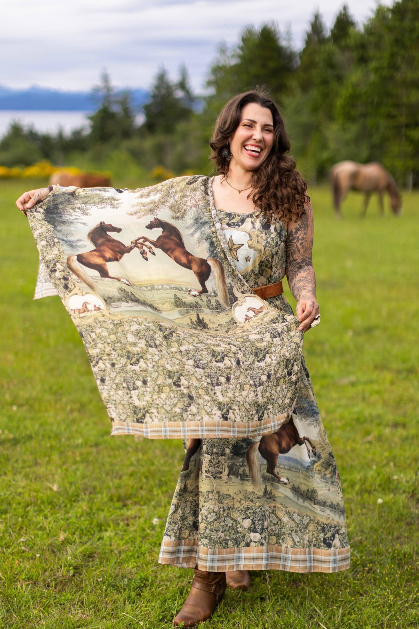 Woman holding a blanket with horse design in a grassy field with horses in the background