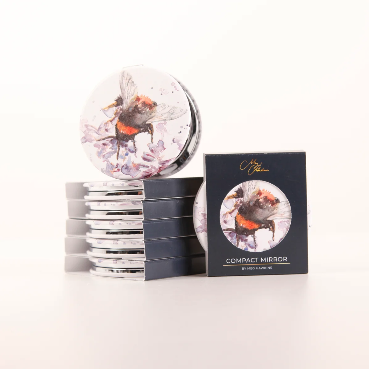 A stack of compact mirrors with a bumblebee illustration on the lid, displayed next to its dark navy blue packaging box on a clean white background.