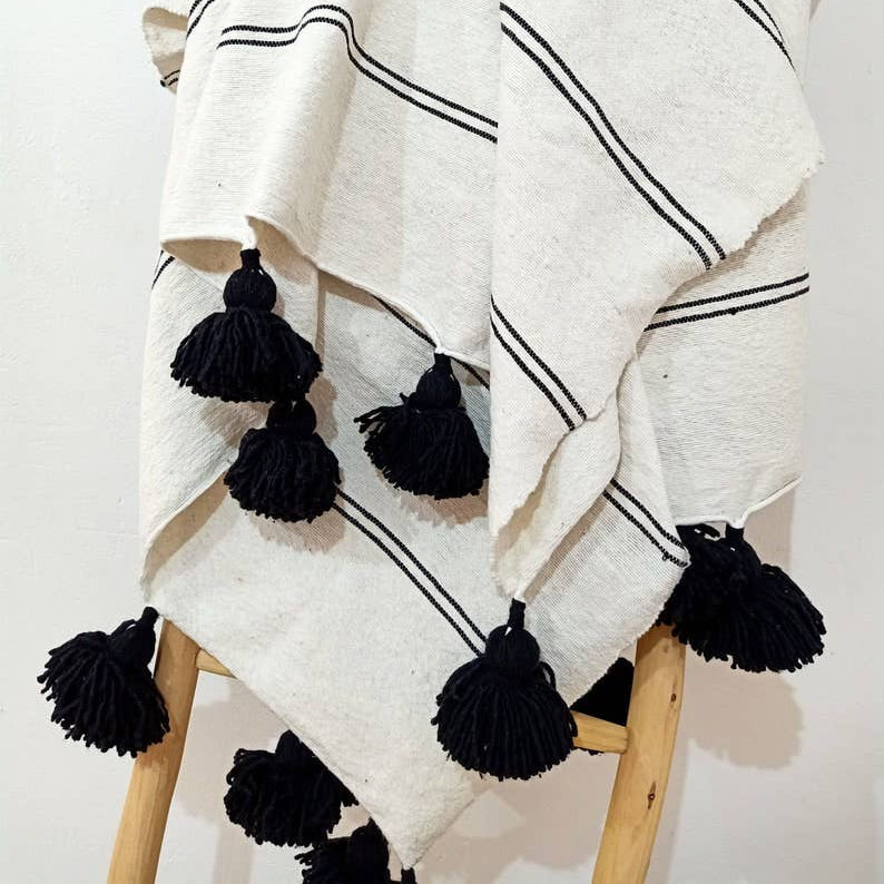 White blanket with black stripes and tassels draped over a wooden chair on a white background