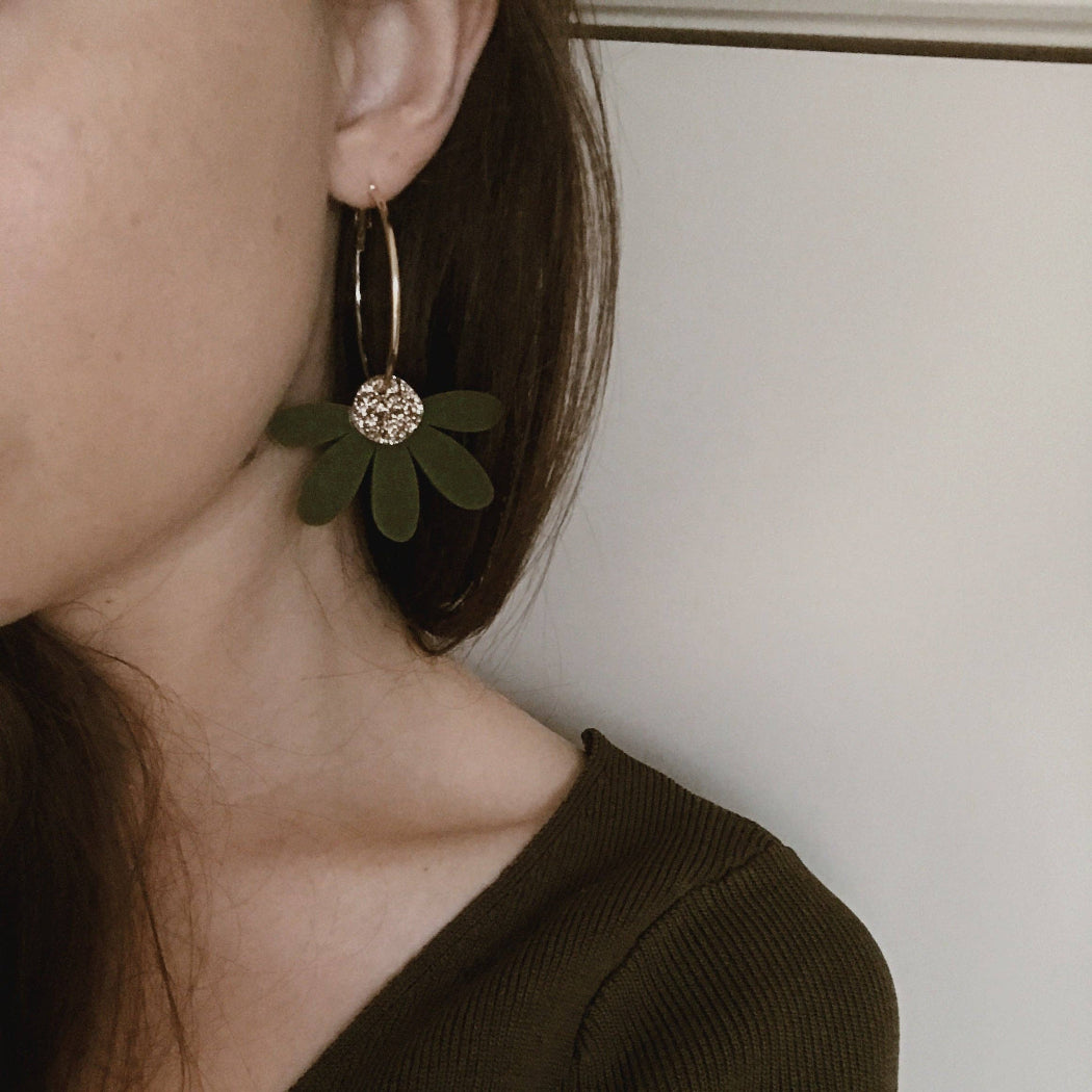 Close-up of a person wearing a green floral earring with a white background