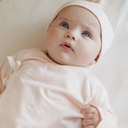 Baby in a pink outfit and headband lying on a white blanket