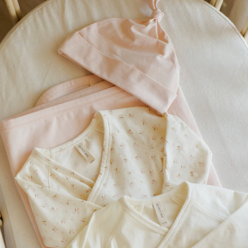 Baby clothing set with pink and cream outfits on a white surface