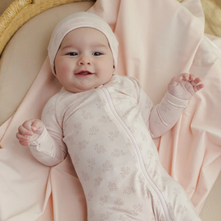 Baby in a pink outfit and headscarf lying on a pink blanket