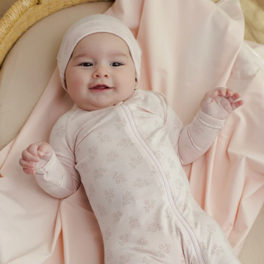 Baby in a pink outfit and headscarf lying on a pink blanket
