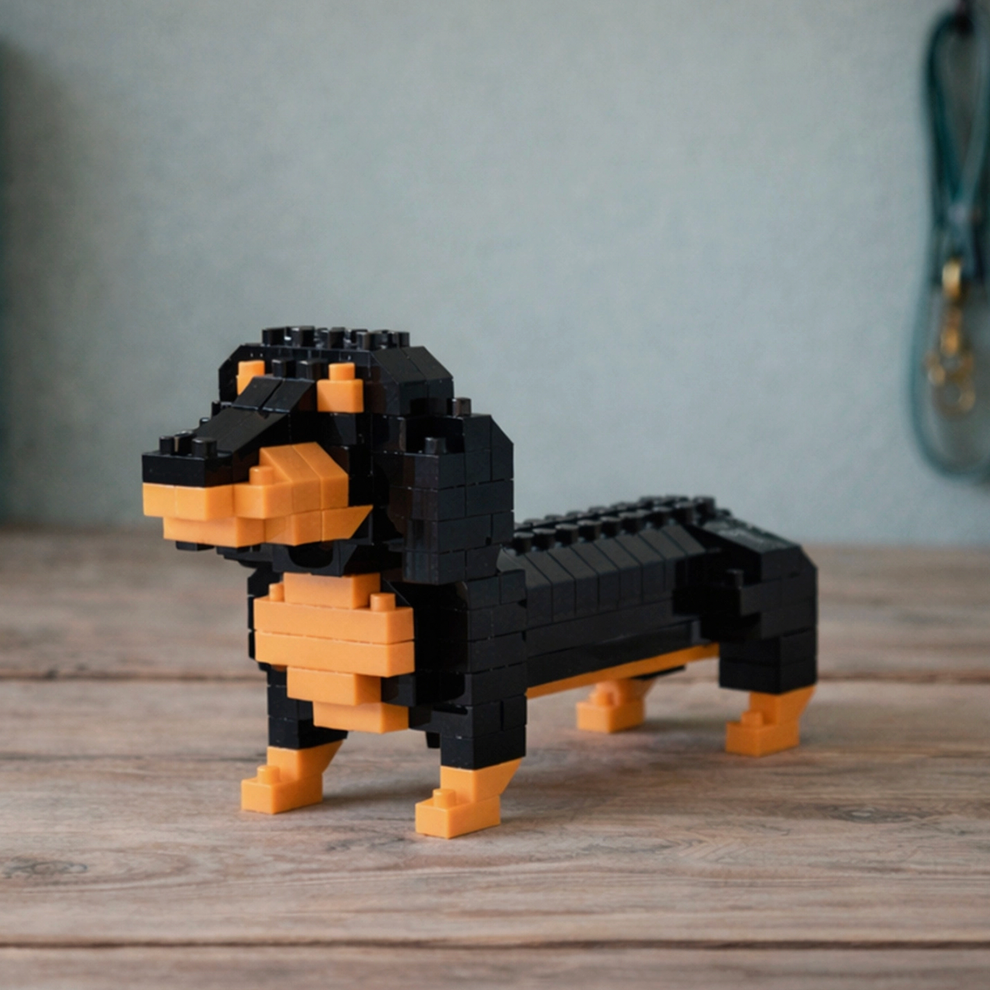 Toy dachshund made of black and orange building blocks on a wooden surface.