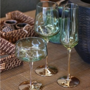 Three capri green glass wine glasses on a wooden surface with wicker baskets in the background.