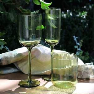 Two green wine glasses with white wine on a wooden table outdoors.