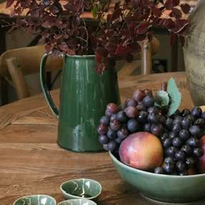 Green pitcher and bowl with grapes and apples on a wooden table
