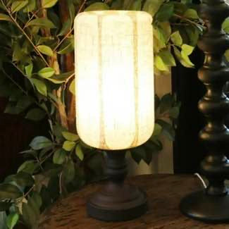 Decorative table lamp with a textured shade on a wooden surface surrounded by greenery