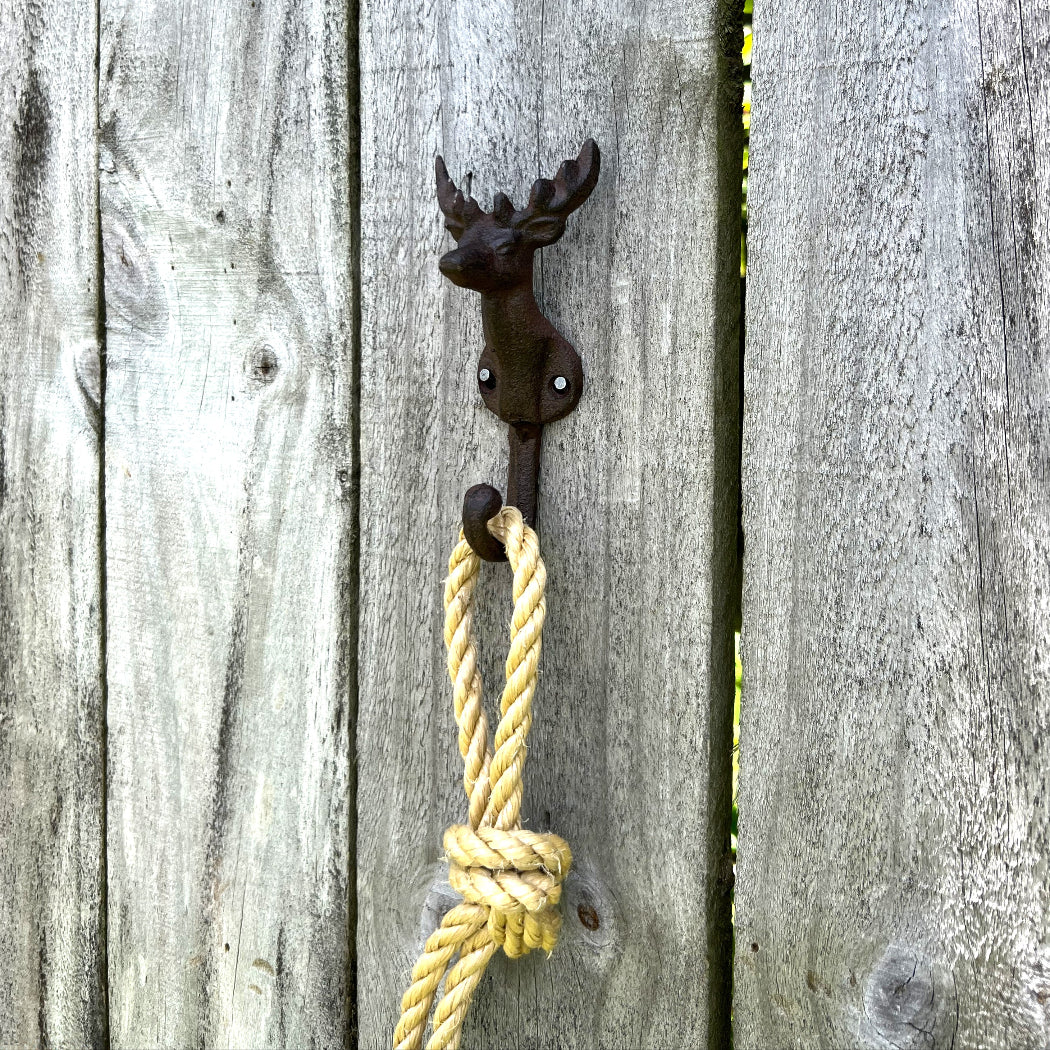 A rustic black metal deer head wall hook mounted on weathered gray wooden fence boards, with a knotted yellow rope hanging from it.
