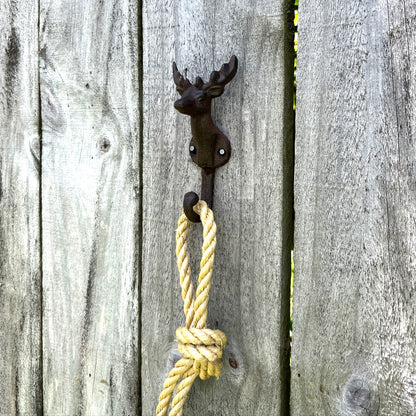 A rustic black metal deer head wall hook mounted on weathered gray wooden fence boards, with a knotted yellow rope hanging from it.