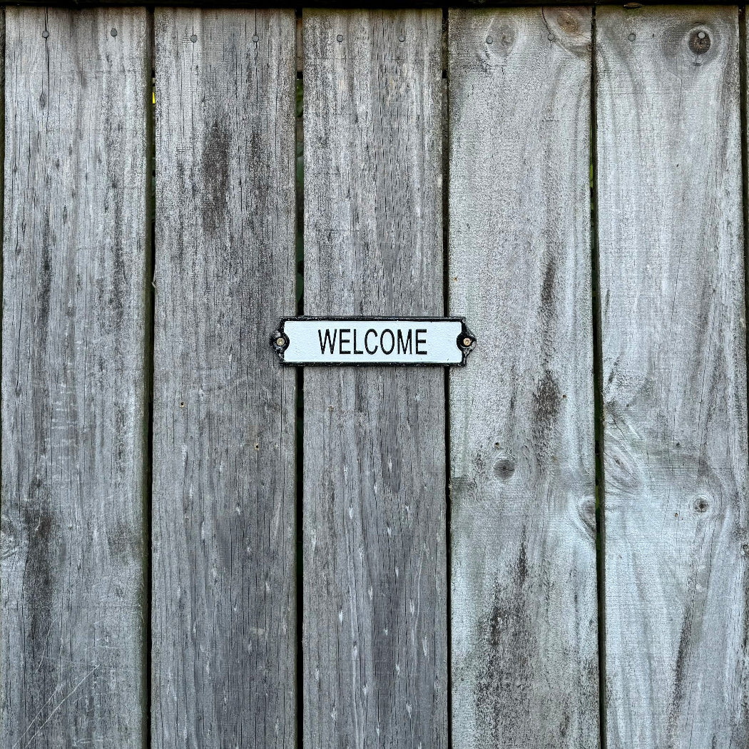 A cast iron welcome sign screwed on a wooden fence