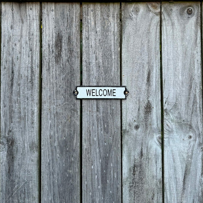 A cast iron welcome sign screwed on a wooden fence