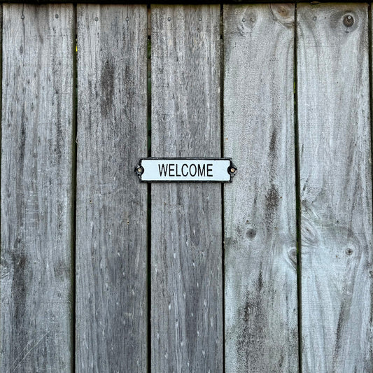 A cast iron welcome sign screwed on a wooden fence