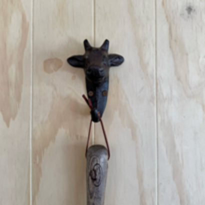 Decorative hook shaped like a cow on a wooden wall.