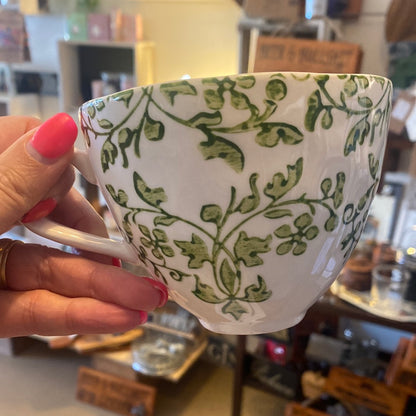 Two hand-painted Florentine cups, one with a green floral pattern and the other with a black floral pattern, both on a white background.