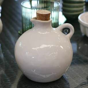 White ceramic bottle with cork stopper on a reflective surface