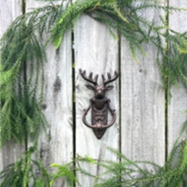 Decorative bottle opener with deer design on a wooden wall surrounded by greenery