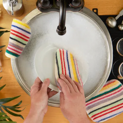 Person cleaning a pot with a colorful striped sponge in a kitchen sink.