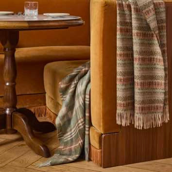 Plaid blanket draped over a wooden chair in a cozy room with a wooden table.