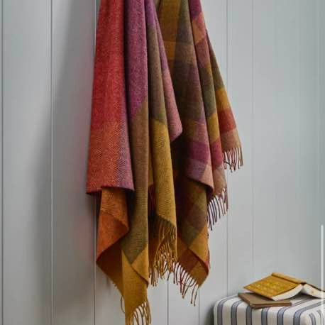 Multicolored plaid blanket hanging on a white wall with a striped stool and books below.