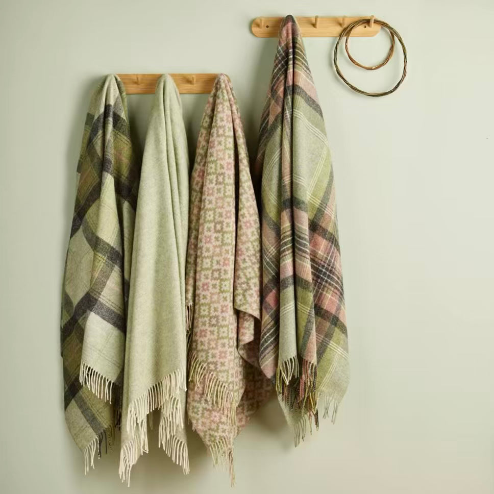 Four plaid throws hanging on a wooden rack against a light background