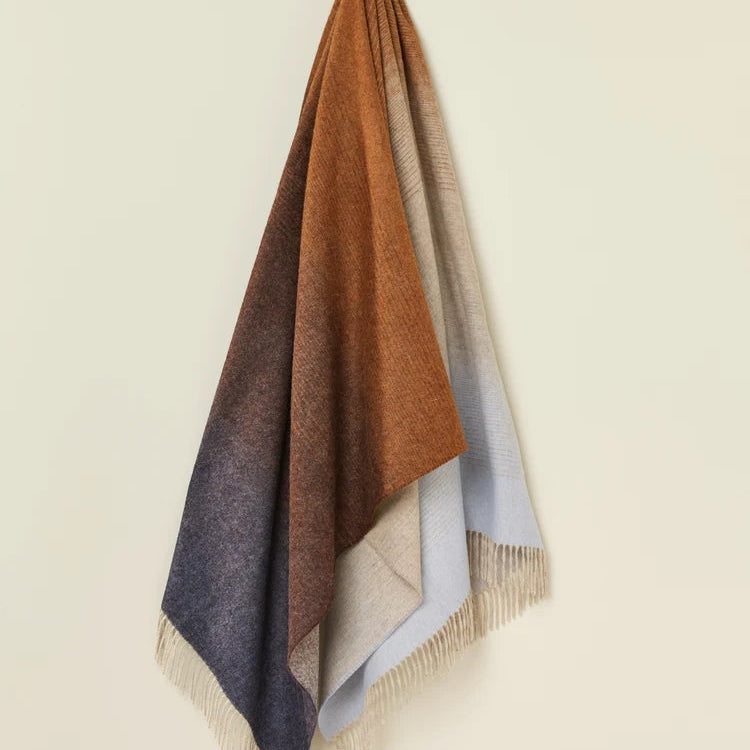 Woven blanket with gradient colors draped over a light beige surface