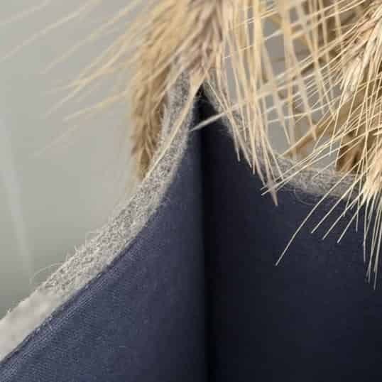 A gray felted wool shopping bag with beige handles placed on a sofa next to a cushion.