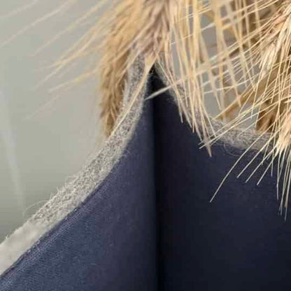 A gray felted wool shopping bag with beige handles placed on a sofa next to a cushion.