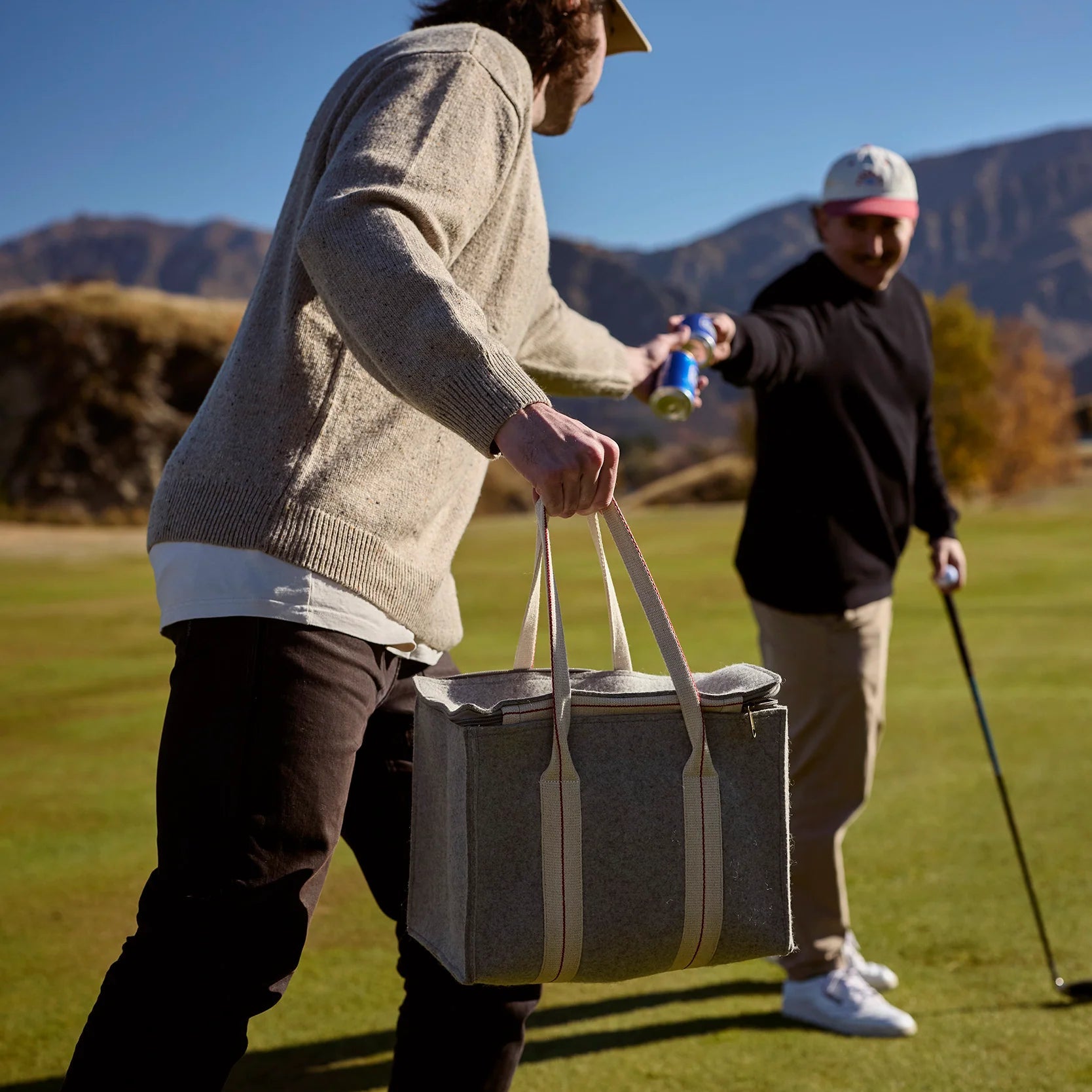 Two people on a golf course with one carrying a cooler.