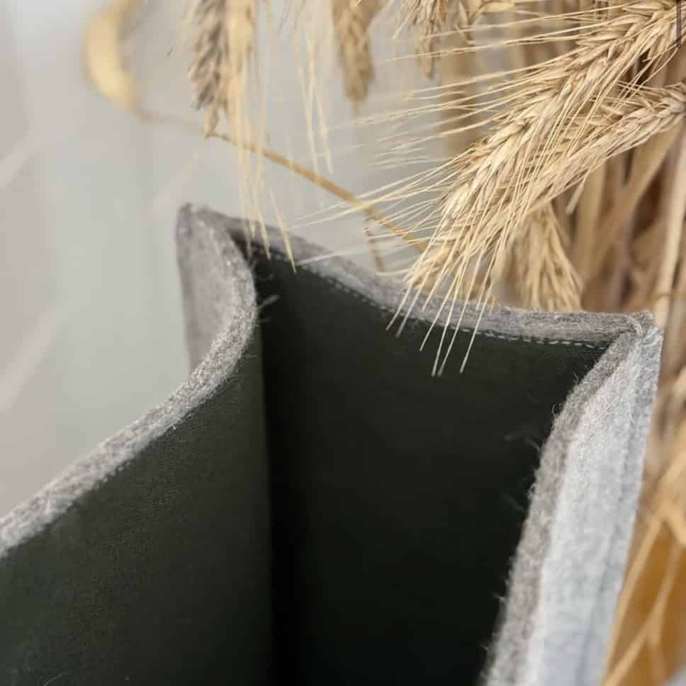 A gray felted wool shopping bag with beige handles placed on a sofa next to a cushion.
