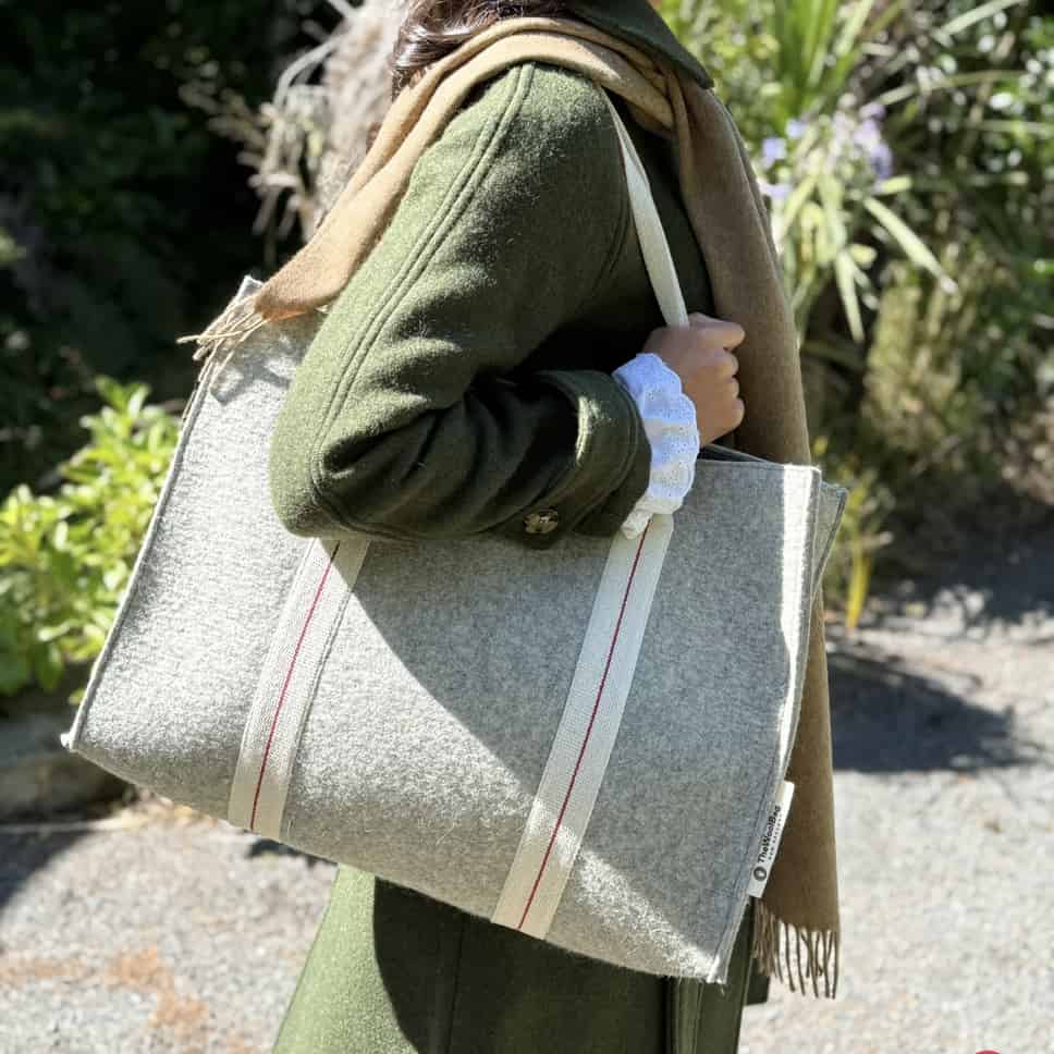 Person holding a textured tote bag outdoors with greenery in the background