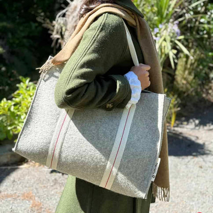 Person holding a textured tote bag outdoors with greenery in the background