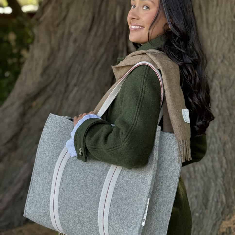 Woman holding a gray tote bag with a tree in the background